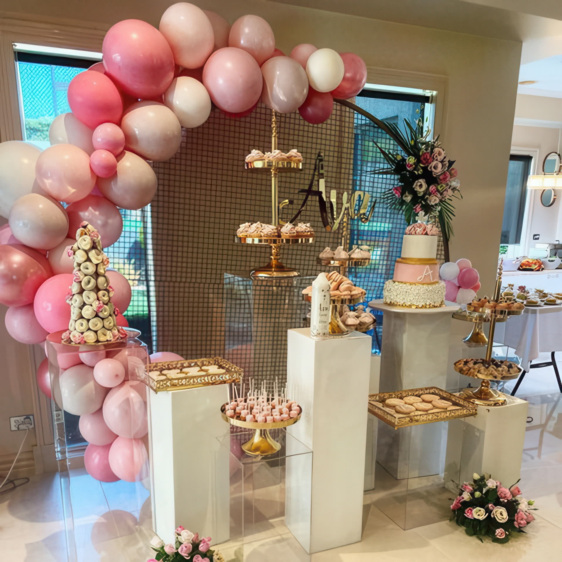 Styled dessert table with tiered stands, sweets and soft pink balloons